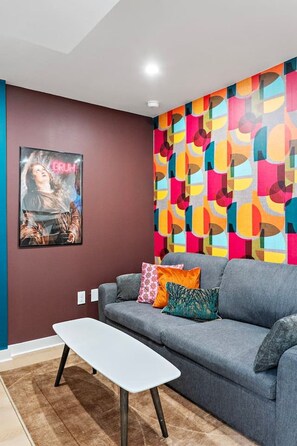 A modern living room with a grey sofa, colorful abstract wall art, and a framed picture on the wall. - Designer 1BR Suite | Trendy Montrose (Houston)