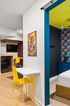 A modern room with a white desk, yellow chairs, a painting, and a bed with a patterned headboard. - Designer 1BR Suite | Trendy Montrose (Houston)