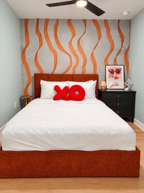 Ein Schlafzimmer mit einem Bett, einem Nachttisch, einem gerahmten Bild und einem Deckenventilator.