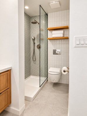 Ein Badezimmer mit einer Duschkabine, einer Toilette und einem Holzboden mit Handtüchern.