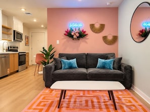 Ein modernes Wohnzimmer mit einem grauen Sofa, einem weißen Couchtisch und einem leuchtend orangefarbenen Teppich.