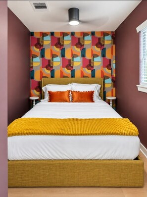 A bed with a white mattress and a mustard-colored headboard, a patterned wall, and a ceiling light fixture. - 1BR | DT Houston | Sleeps 4 (Houston)