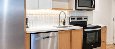 Una cocina moderna con electrodomésticos de acero inoxidable, armarios de madera y salpicadero de azulejos blancos.