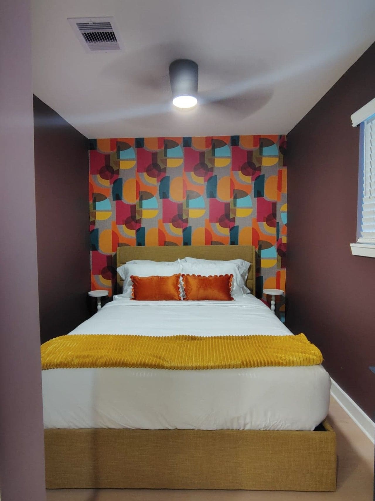A hotel room with a bed, a ceiling fan, and a patterned wall.
