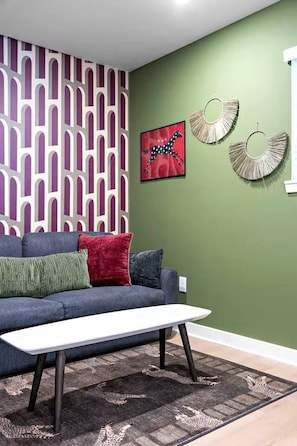 A living room with a sofa, a coffee table, a patterned rug, and wall art. - Designer 1BR | Sleeps 4 | Near DT (Houston)