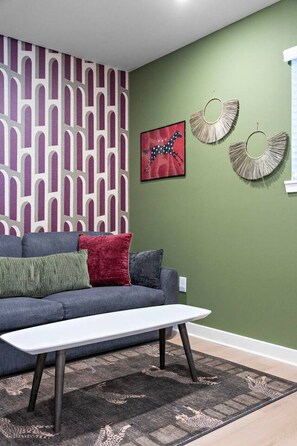 A living room with a grey sofa, a white coffee table, a patterned rug, and wall art. - Designer 1BR | Sleeps 4 | Near DT (Houston)