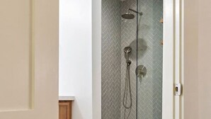 A modern bathroom with a glass-enclosed shower, a wooden cabinet, and a white door. - Designer 1BR | Sleeps 4 | Near DT (Houston)