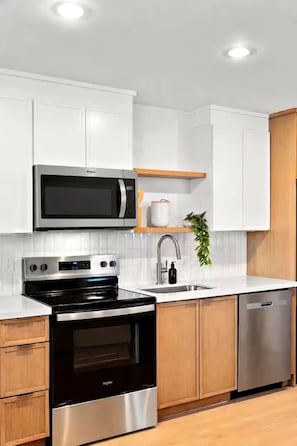 A modern kitchen with white cabinetry, a stainless steel microwave, oven, and dishwasher, and a wooden countertop. - Designer 1BR | Sleeps 4 | Near DT (Houston)