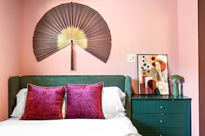 A bed with two pillows, a bedside table with a lamp, and a wall-mounted fan. - Designer 1BR | Sleeps 4 | Near DT (Houston)