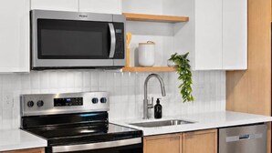 A modern kitchen with white cabinetry, a stainless steel microwave, oven, and dishwasher, and a wooden countertop. - Designer 1BR | Sleeps 4 | Near DT (Houston)