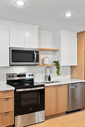A modern kitchen with white cabinetry, a stainless steel microwave, oven, and dishwasher, and a wooden countertop. - Designer 1BR | Sleeps 4 | Near DT (Houston)