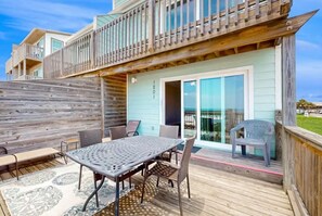 A deck with a table and chairs, a wooden fence, and a building with a balcony. - The Breeze (Gulf Shores)