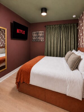 A bedroom with a bed, a television displaying 'NETFLIX,' a wall-mounted picture of horseshoes, and a window with curtains. - Trendy 1BR + Sofa Bed | Sleeps 4 (Houston)