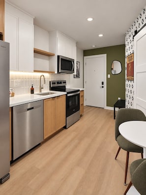 A modern kitchen with white cabinets, stainless steel appliances, and a wooden floor. - Trendy 1BR + Sofa Bed | Sleeps 4 (Houston)