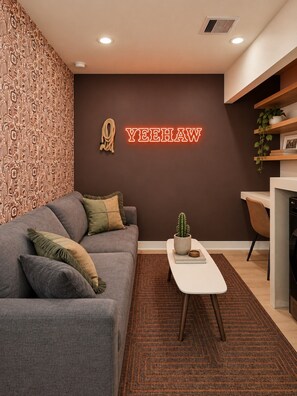 A modern living room with a grey sofa, a small coffee table, and a wall-mounted neon sign. - Trendy 1BR + Sofa Bed | Sleeps 4 (Houston)