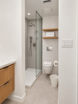 A modern bathroom with a glass-enclosed shower, a toilet, a sink, and a white tiled wall. - Trendy 1BR + Sofa Bed | Sleeps 4 (Houston)