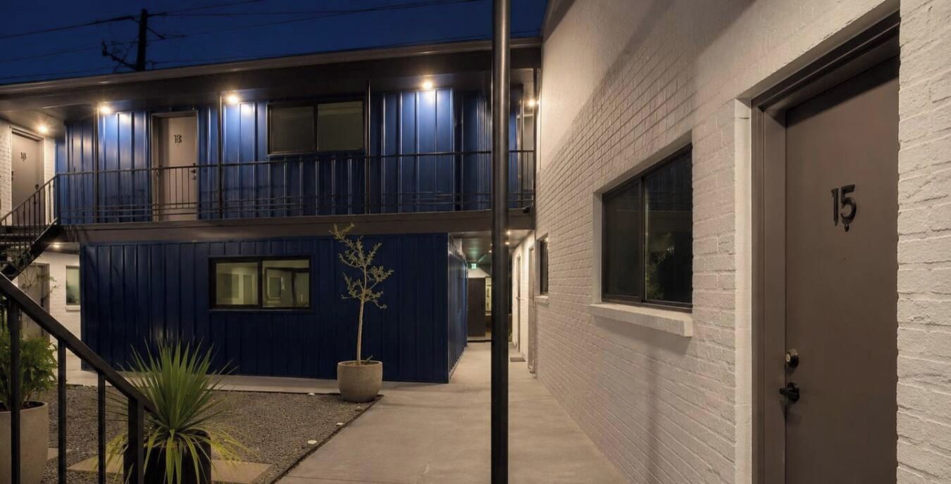 Un edificio con fachada azul, una puerta blanca con el número 15 y un pequeño árbol en una maceta.