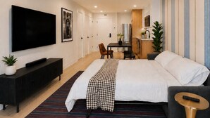 Une chambre d’hôtel moderne dotée d’un grand lit, d’une télévision, d’un coin repas et d’une kitchenette.