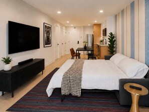 Ett modernt hotellrum med en stor säng, en TV, en matplats och ett litet kök.