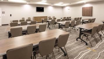 A conference room with multiple tables and chairs, a flat-screen TV mounted on the wall, and a wooden panel on the back wall.