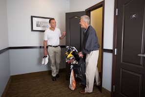 Dos homes en un passadís, un portant sabates i una borsa de golf, l'altre portant una borsa de golf.