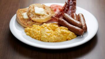 A plate with scrambled eggs, sausages, bacon, and toast with butter.