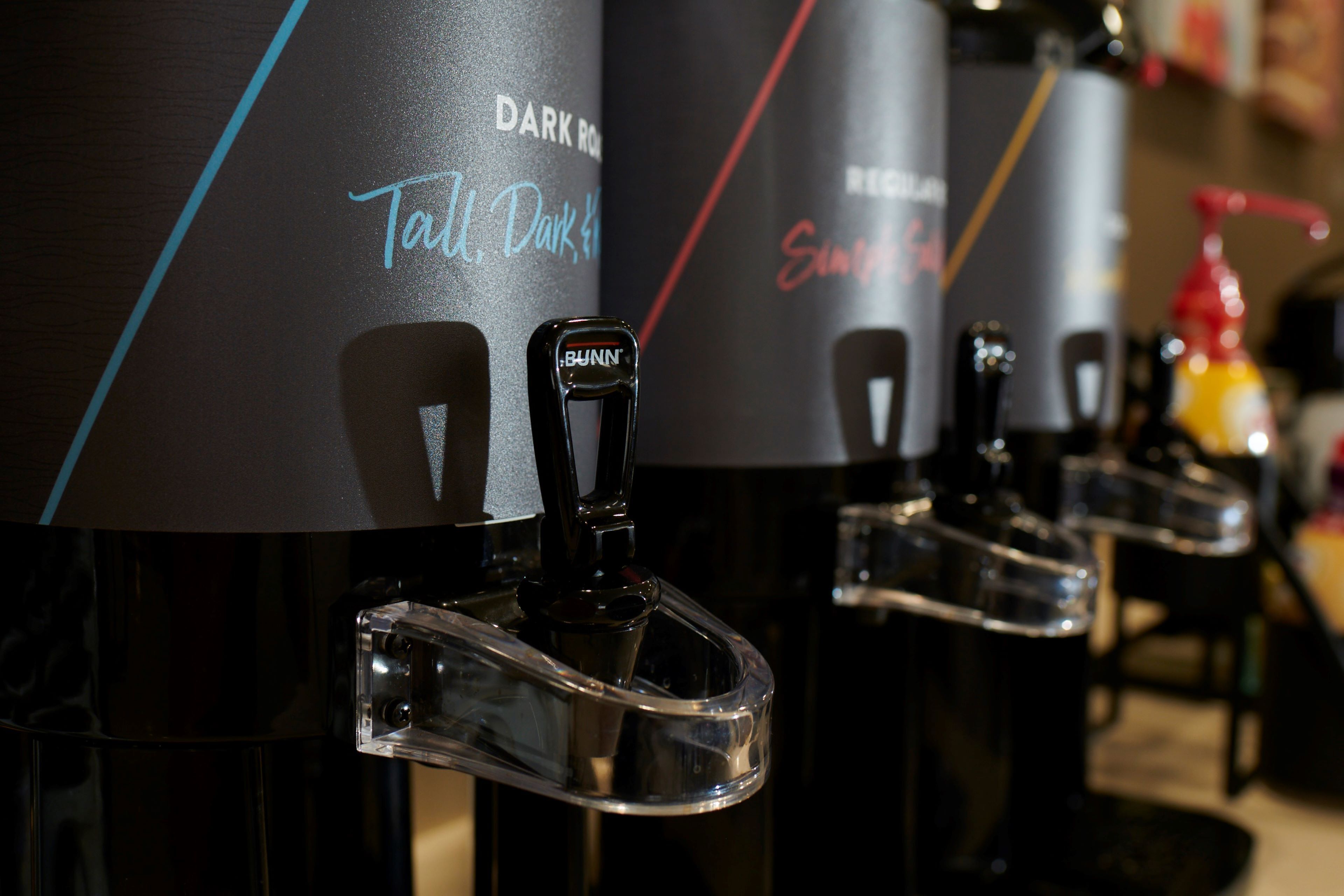 Una fila de dispensadores de bebidas con etiquetas que indican distintas opciones.