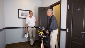 Two men in a hallway, one holding shoes and a golf bag, another holding a golf bag. - Accessible 1BR w/ 2 Queens | Hot Breakfast + Pool (Denton)