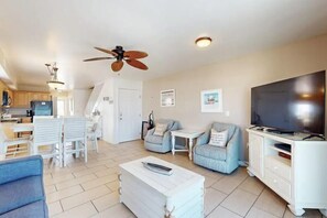 A modern living room with a ceiling fan, a flat-screen TV, and a dining area with a table and chairs. - Alabama Breeze (Gulf Shores)