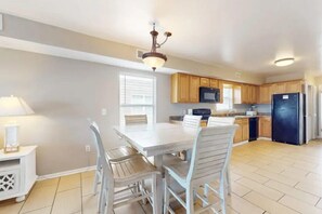 A kitchen with a dining table, chairs, cabinets, a refrigerator, and a microwave. - Alabama Breeze (Gulf Shores)