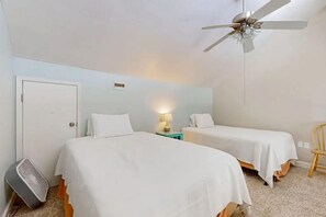A bedroom with two beds, a ceiling fan, a heater, and a small table with a lamp. - Alabama Breeze (Gulf Shores)