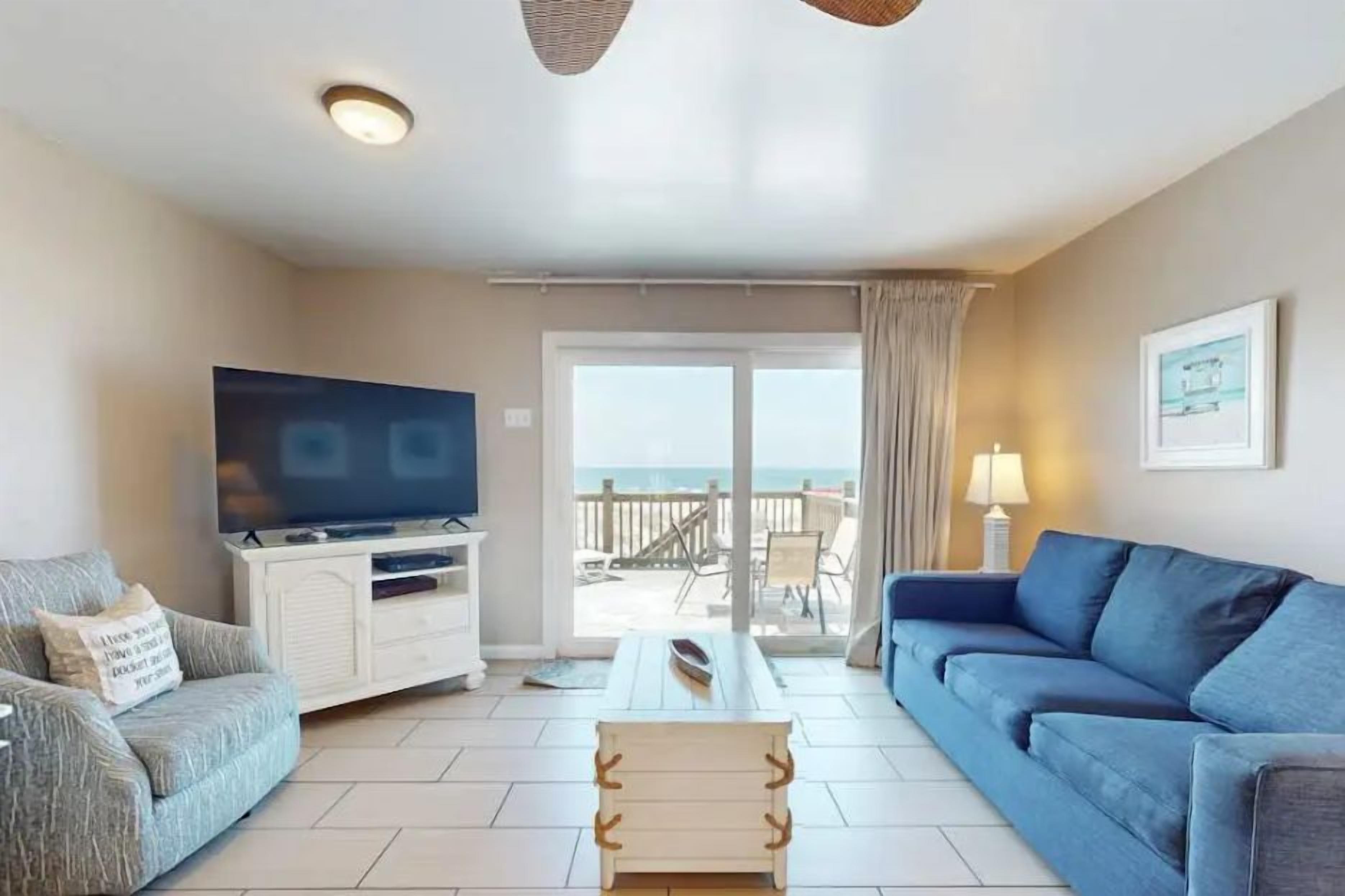 A living room with a television, sofa, and a view of the outdoors.