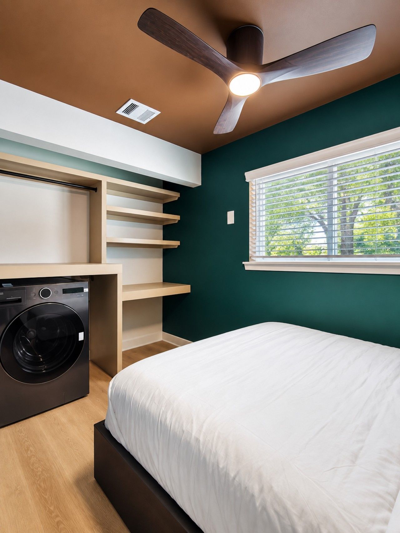 A compact room with a bed, built-in shelving, a washing machine, and a ceiling fan.