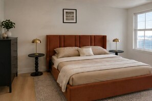 Ein Schlafzimmer mit einem Bett, Nachttischen, einer Kommode, einem Fenster und einem gerahmten Bild an der Wand.