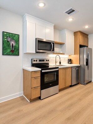 A modern kitchen with white cabinetry, stainless steel appliances, and a wooden floor. - 1BR Designer Suite | Sleeps 4 (Houston)