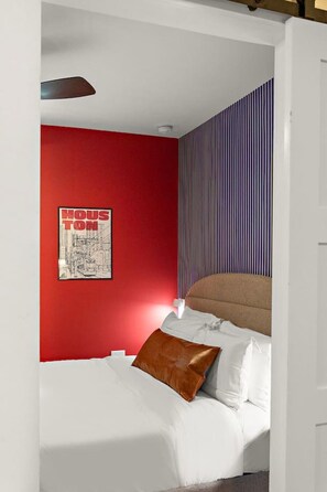 A bedroom with a red wall, a striped wallpaper, a bed with white bedding and a brown pillow, and a framed picture on the wall. - Trendy 1BR | DT Houston | Sleeps 4 (Houston)