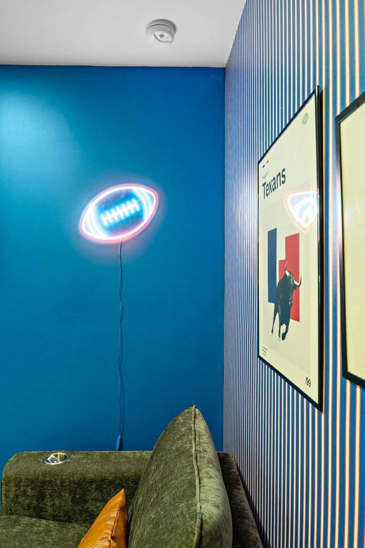 Une pièce avec un mur bleu, une affiche encadrée, un panneau lumineux et un canapé.