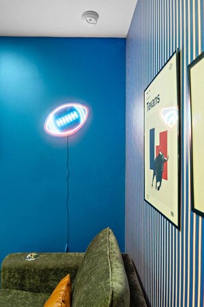 A room with a blue wall, a framed poster, a neon sign, and a couch. - Trendy 1BR | DT Houston | Sleeps 4 (Houston)