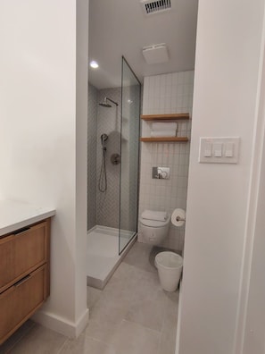 A bathroom with a glass-enclosed shower, a toilet, and a sink with a wooden cabinet. - Modern 1BR | Free Parking | Sleeps 4 (Houston)