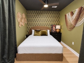 A bedroom with a bed, a ceiling fan, a wall with a geometric pattern, and a hanging macrame. - Modern 1BR | Free Parking | Sleeps 4 (Houston)