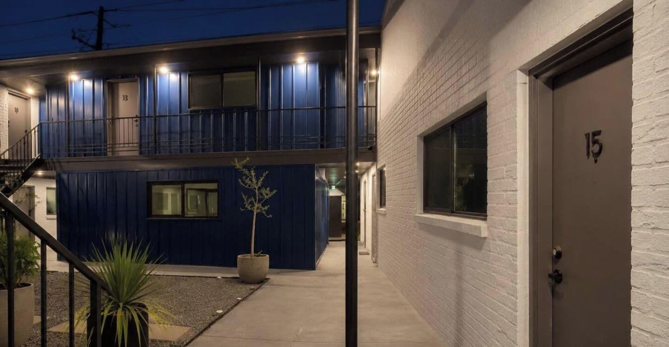 Ein zweistöckiges Gebäude mit blauer Fassade, einer weißen Tür mit der Aufschrift '15' und einem kleinen Blumentopf im Vordergrund.