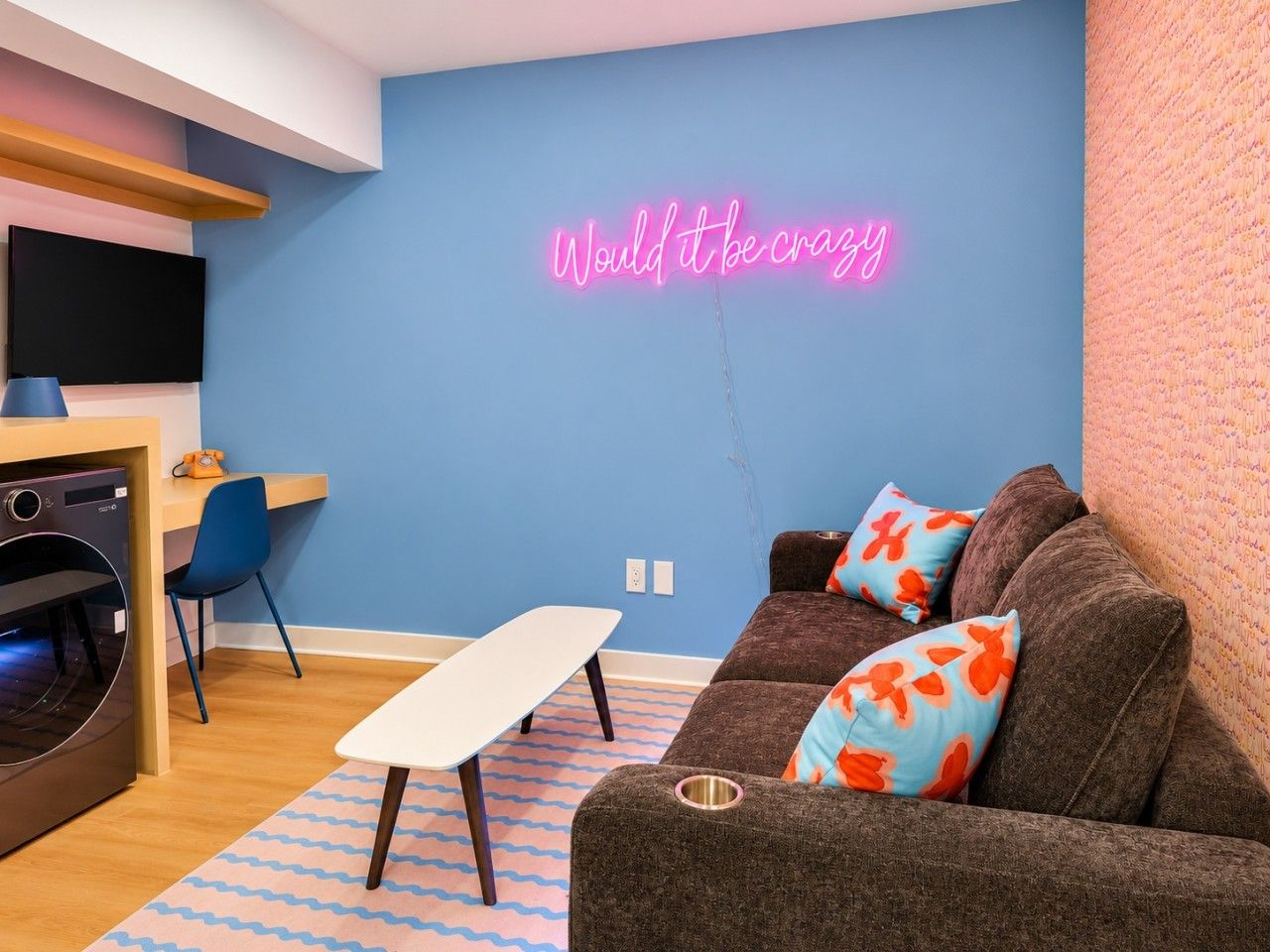 A modern living room with a neon sign, a sofa, a table, and a TV.