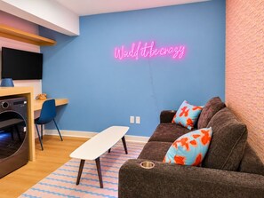 A modern living room with a neon sign, a sofa, a table, and a TV. - Modern 1BR Suite + Sofa Bed | Sleeps 4 (Houston)