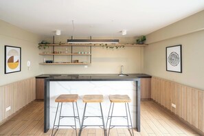 A modern kitchen with a central island, bar stools, and shelves with kitchenware. - La Buenavista Prado Residences (La Victoria)