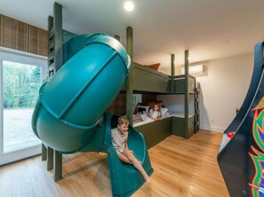 A room with a green slide, bunk beds, and a window with a view of trees. - Heated Pool, Hot Tub, Fire Pit & Outdoor Theater - Asheville" (Fairview)