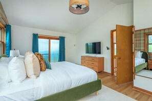 A bedroom with a bed, a dresser, a television, and a door leading to another room. - Heated Pool, Hot Tub, Fire Pit & Outdoor Theater - Asheville" (Fairview)