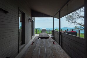 A covered porch with a wooden bench and a grill, overlooking a scenic view with mountains and a body of water. - Heated Pool, Hot Tub, Fire Pit & Outdoor Theater - Asheville" (Fairview)