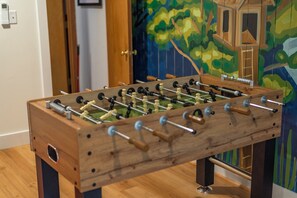 A wooden foosball table with a clear view of the rods and figures, set against a wall with a colorful mural. - Heated Pool, Hot Tub, Fire Pit & Outdoor Theater - Asheville" (Fairview)