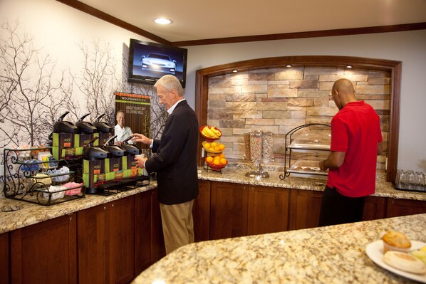 Un bar à petit-déjeuner avec des machines à café, un présentoir de fruits et un mur en pierre en arrière-plan.