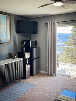 Ein moderner Wohnraum mit Flachbildfernseher an der Wand, einem integrierten Wasserspender, einem Kühlschrank und Blick auf eine Berglandschaft durch ein großes Fenster.